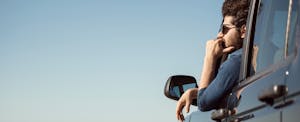 auto-loan-refinancing-myths A man wearing sunglasses leans out of his car window, staring pensively into the distance.