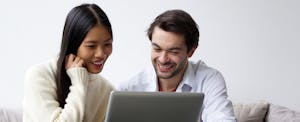 Two people sitting at a desk, using a laptop together and chatting