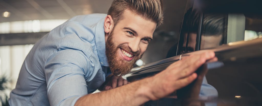 Young man visiting car dealership and coveting car while wondering how he'll finance it.
