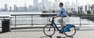 Young businessman biking to work from one state to another, city skyline in the background.