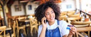Young smiling woman holding a credit card and making purchases online using laptop