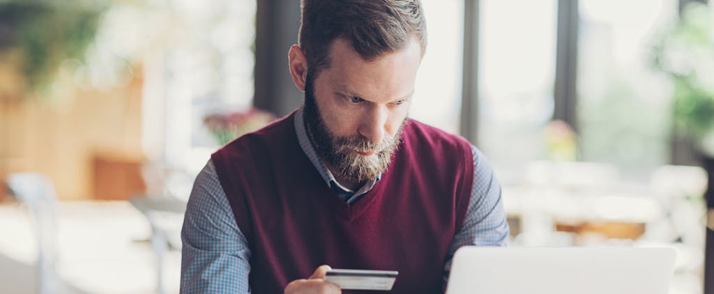 Man with beard holding a credit card and using laptop in cafe