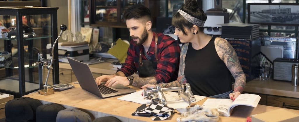 Young tattooed business owners discussing how to pay their self-employment tax.