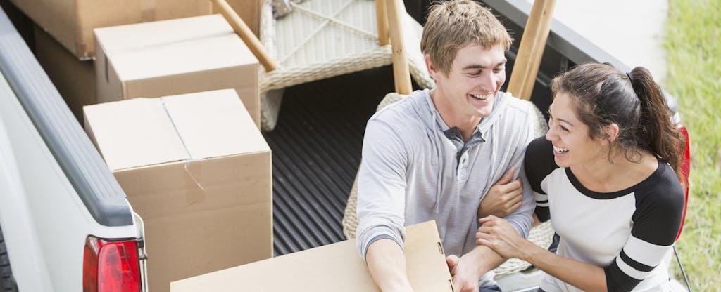 A young man and woman sit in the cab of their moving truck