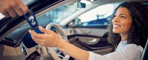 understand-car-loan Woman sits in her new car as the deal hands her the keys