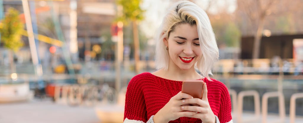 Smiling Young Woman Using Smart Phone While Standing Outdoors