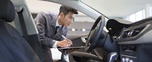 Man looking at a car and taking notes on a clipboard