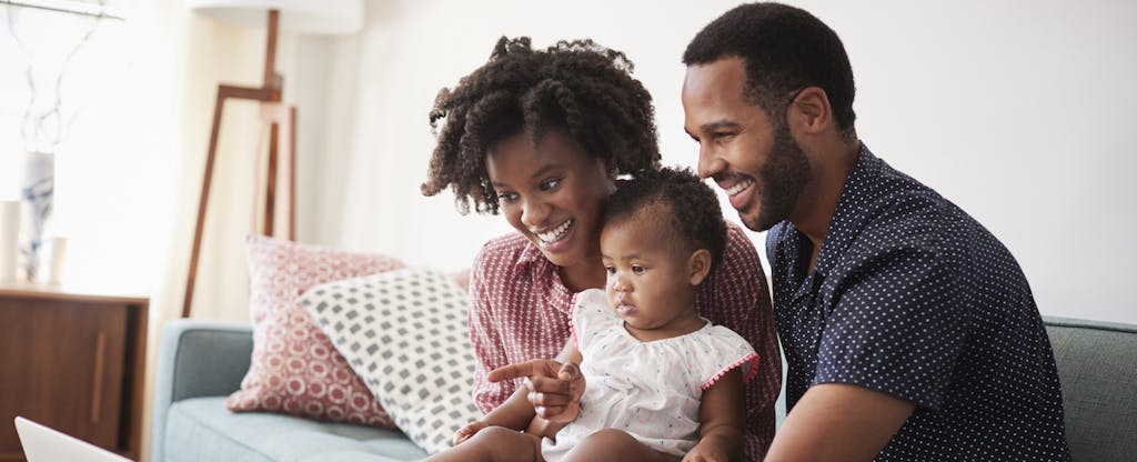 Man and woman sitting on a couch with their baby, looking at a computer together