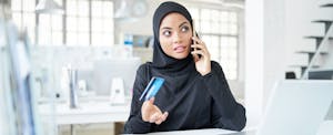 Woman sitting at her desk, holding her credit card and talking on the phone