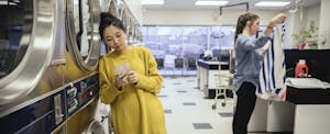 filed-claim-equifax-settlement-provide-info Woman standing in a laundromat, looking at her phone