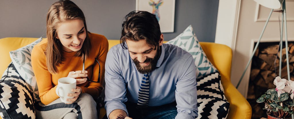 Man and woman sitting together on their couch, smiling and talking to each other about whether to get a HELOC vs. a home equity loan
