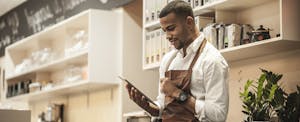 Business owner in his coffee shop looking up loans for self-employed people on his digital tablet