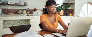 Young woman on laptop at kitchen table, thinking about taking out a 401(k) home loan