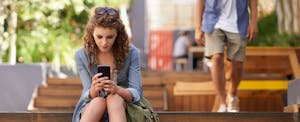 Young woman sitting outside, reading about passive income ideas on her phone