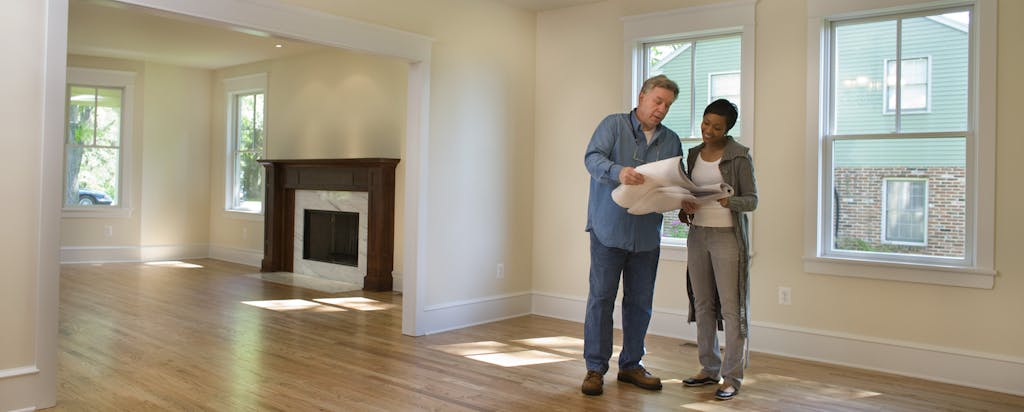 A man and a woman are standing in an empty house, looking over the specs of the home...