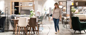 A woman smiles as she looks at a dining set in a furniture showroom.