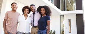 Happy family, with two teenagers, in front of their new home