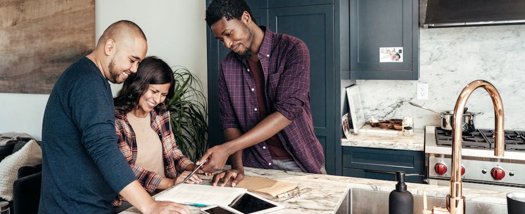A couple reviews plans with a contractor while standing around their kitchen island.