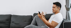 Man stretched out on a sofa, checking his mobile phone