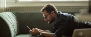 best-auto-insurance-for-high-risk-drivers Man lying on his couch, reading on his phone about the best auto insurance for high-risk drivers