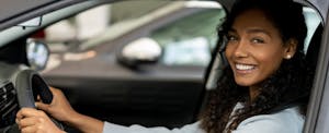 fiesta-auto-insurance-review Young woman smiling at the camera while behind wheel of her car