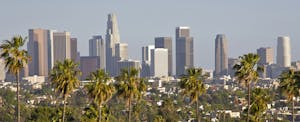 los-angeles-debt-statistics Daytime skyline of downtown Los Angeles, with tall high rise buildings in the background and palm trees in the foreground.