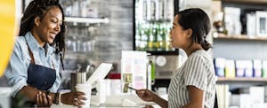 Young woman paying for her coffee at counter with her cash back debit card