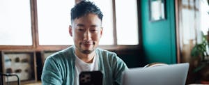 Young Asian man on his mobile phone, smiling as he checks on his TD Bank Checking account