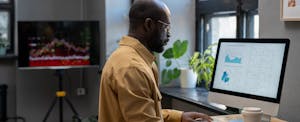 A data scientist sits in a home office in front of a large desktop computer