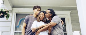 Family standing outside of their new home, embracing each other and smiling