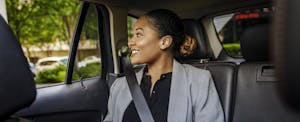 best-rideshare-insurance Professional woman sitting in the backseat of a car, looking out the window.
