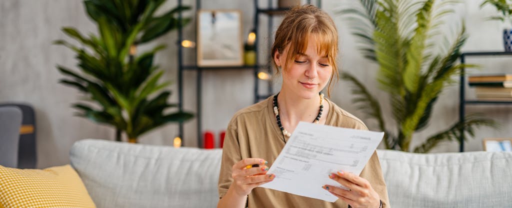 Young woman sits on a couch looking over finances.