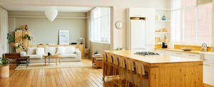 Chairs arranged at kitchen island in apartment. Sofa with coffee table is in living room. Interior of modern bright home.