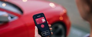 state-auto-insurance-review-1468749546.jpg Over the shoulder view of a person looking at a car app on phone next to red car.